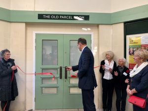 Man cuts ribbon with scissors at opening of former redundant railway station building