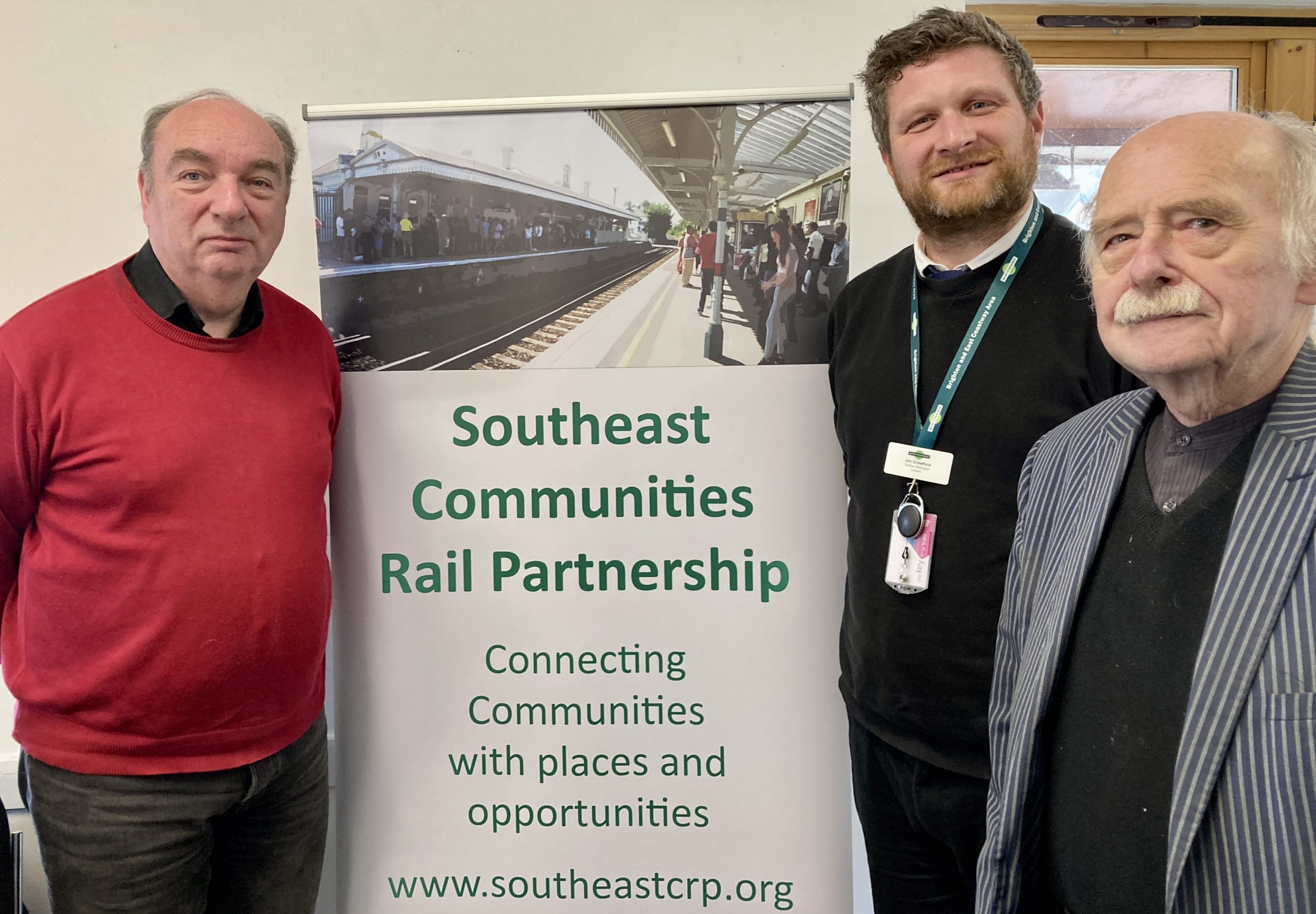 Three men in front of banner displaying information about Community Rail
