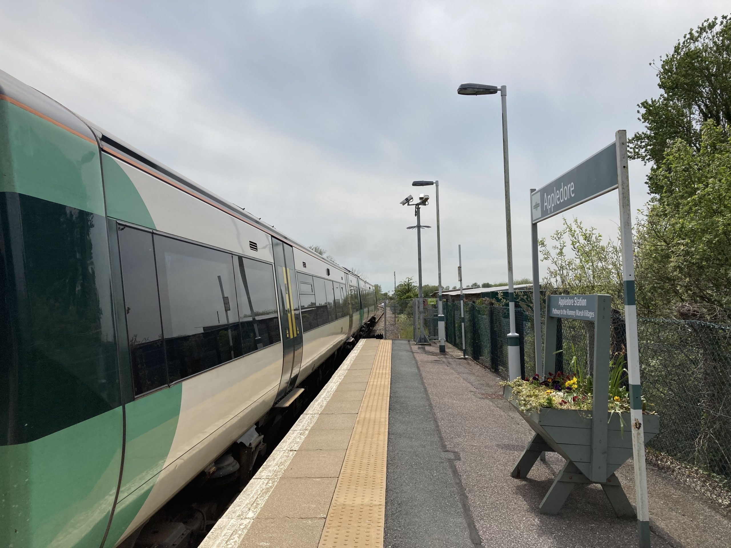Train at station with platform, station sign Appledore and planted flower trough